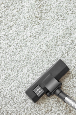 A professional technician operating a commercial hot water extraction carpet machine on blue facility flooring.